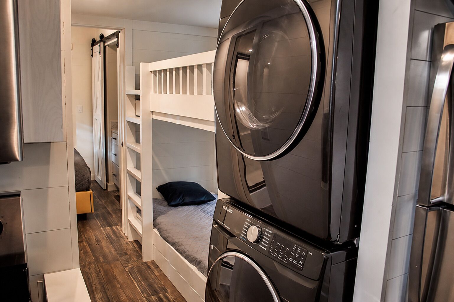 Habitación funcional con una cama litera, lavadora y un pequeño espacio para sentarse.