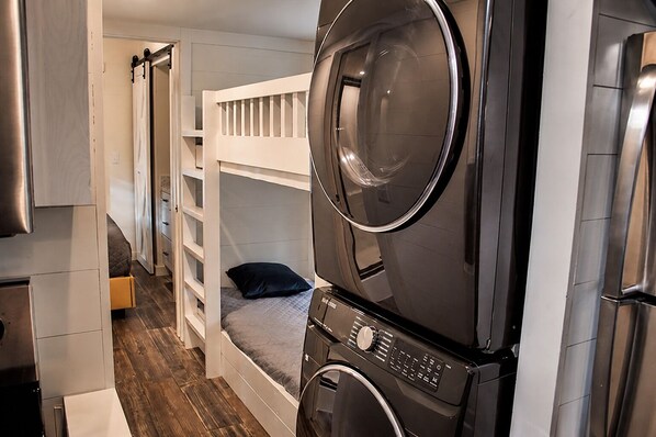 Habitación funcional con una cama litera, lavadora y un pequeño espacio para sentarse.
