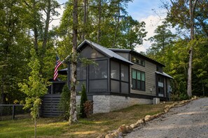A two-story cabin with a stone foundation, large windows, and an American flag.
