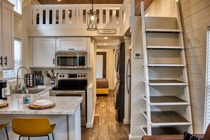 Una cocina con una isla central, microondas, horno, refrigerador y una escalera.