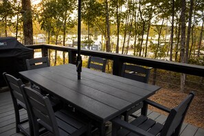 A deck with a table and chairs, overlooking a wooded area and a body of water.