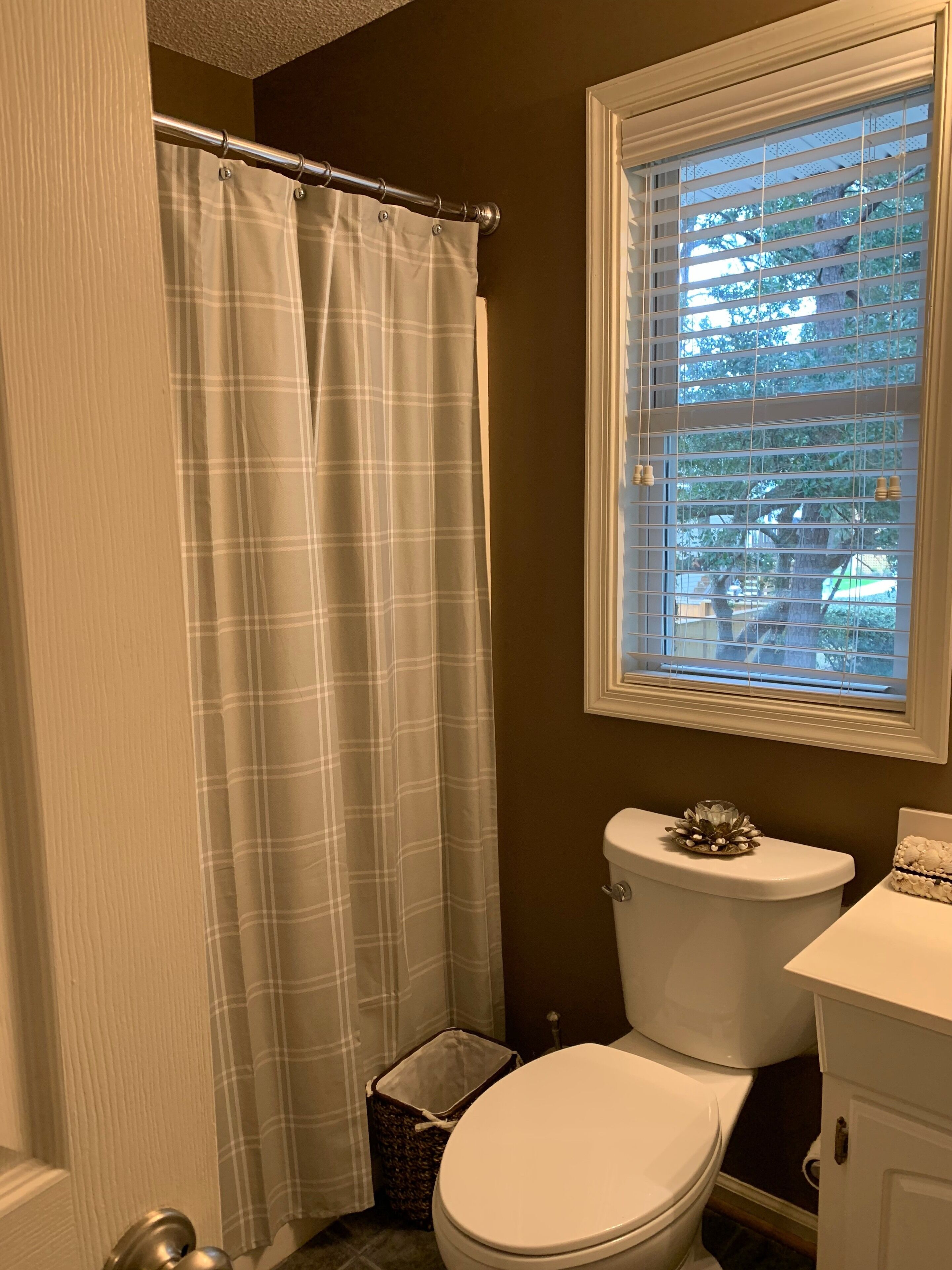 A bathroom with a white toilet, a white sink, a window with blinds, and a shower curtain.