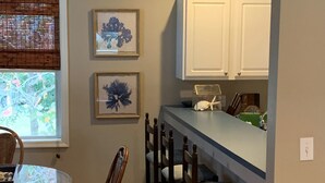 A kitchen with a dining area, wooden chairs, a round table, and framed artwork on the wall. - Private, Spacious Beach Retreat with Fenced in Shaded Yard (Kill Devil Hills)