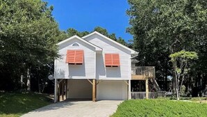 A two-story house with a garage, surrounded by trees and a well-maintained lawn. - Private, Spacious Beach Retreat with Fenced in Shaded Yard (Kill Devil Hills)