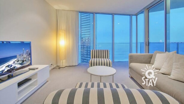 Una sala de estar moderna con televisor, sofá, sillón y reposapiés.