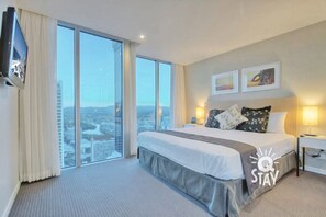 Enjoy a panoramic city view from the comfort of this stylish room, featuring a large bed, two bedside tables, and a flat-screen TV.