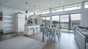 Een moderne keuken met witte kasten, een eethoek met barkrukken en grote ramen met uitzicht op de omgeving.