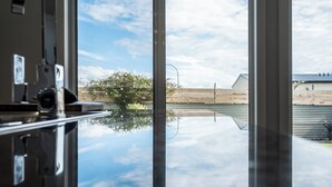 Een kamer met een groot raam dat een heldere lucht en een ver weids uitzicht op een brug en bomen weerspiegelt.