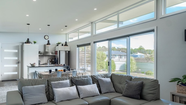 Een moderne woonkamer met een grijze modulaire bank, een eethoek en een keuken met witte kasten en roestvrijstalen apparatuur.