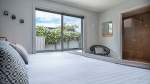 Een slaapkamer met een groot bed, een stoel, een schuifglazen deur naar een balkon en een douche.