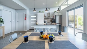 Een moderne keuken met een centraal eiland, een eethoek met een tafel gedekt voor vier personen, en grote ramen die natuurlijk licht binnenlaten.