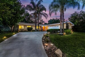 A residential house with a driveway, palm trees, and a well-maintained lawn.