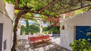 Zona de dinar a l'aire lliure coberta amb una taula per a dos, envoltada d'arbres en testos i vista al mar.