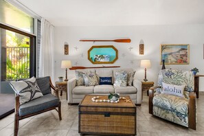 Una sala de estar con un sofá, sillones, una mesa de centro y elementos decorativos como una estrella de mar y una fotografía de una playa.