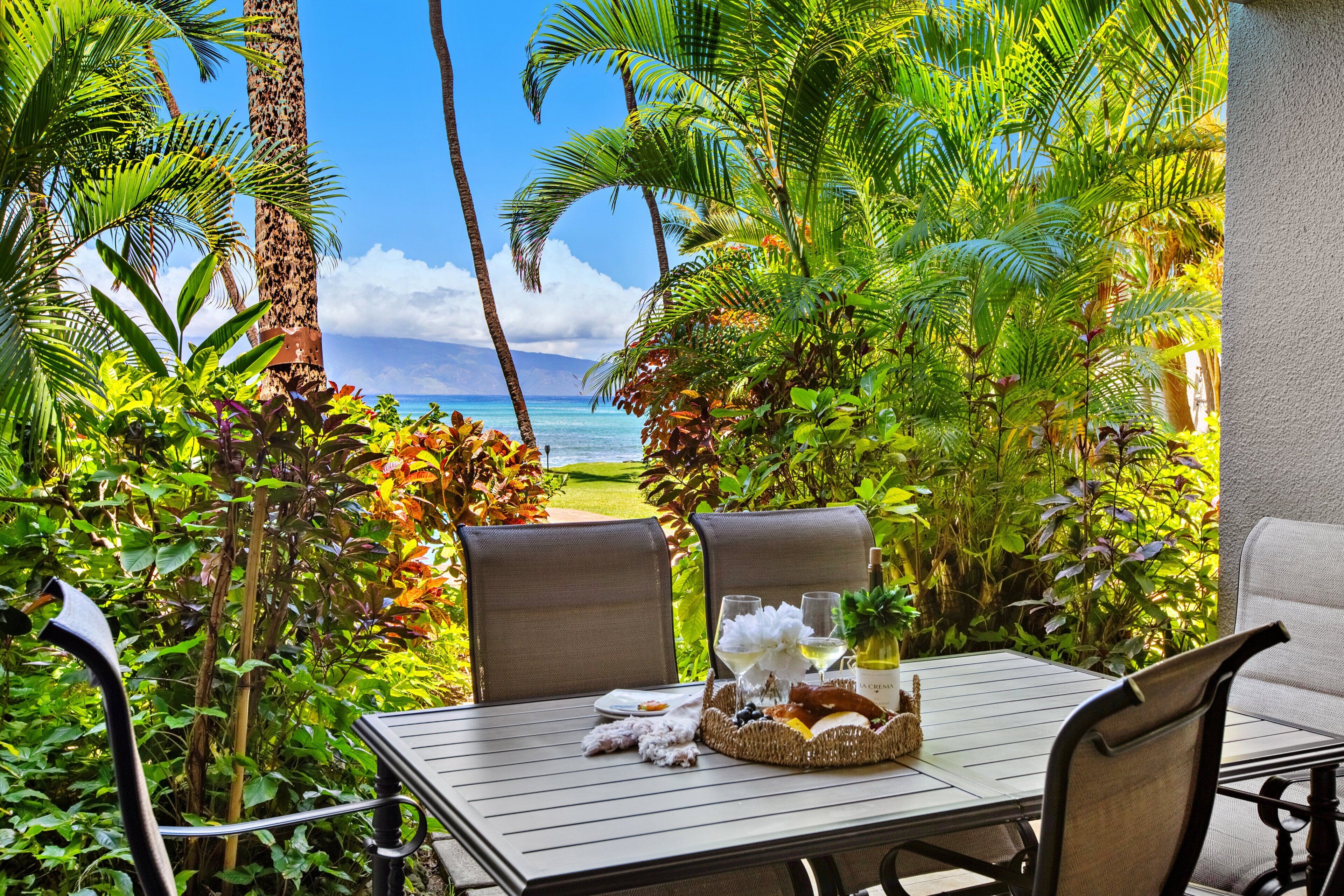 Une table installée à l’extérieur, avec des chaises, donnant sur l’océan et entourée d’une végétation tropicale.