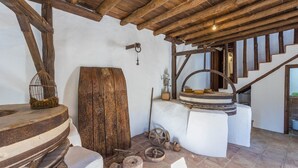 Et rustikt interiør med træbjælker, en stor trædør, en stenvæg og en trappe med trætrin.