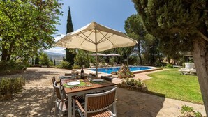 Uma área de refeições ao ar livre com mesa posta para dois, piscina e gramado.