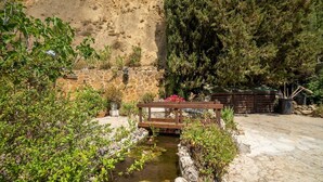 Um jardim com lago pequeno, ponte de madeira e muro de pedra.