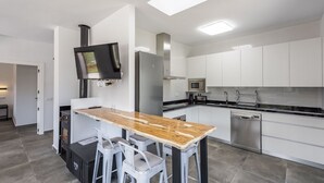 A modern kitchen with white cabinets, a stainless steel refrigerator, a microwave, and a dishwasher. There is a wooden table with two chairs and a TV mounted on the wall. - Cortijo Villa Maroma Órgiva by Ruralidays (Granada)