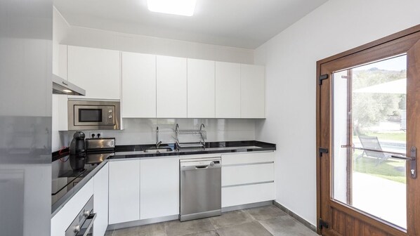 A modern kitchen with white cabinets, a stainless steel dishwasher, a microwave, and a black countertop. - Cortijo Villa Maroma Órgiva by Ruralidays (Granada)
