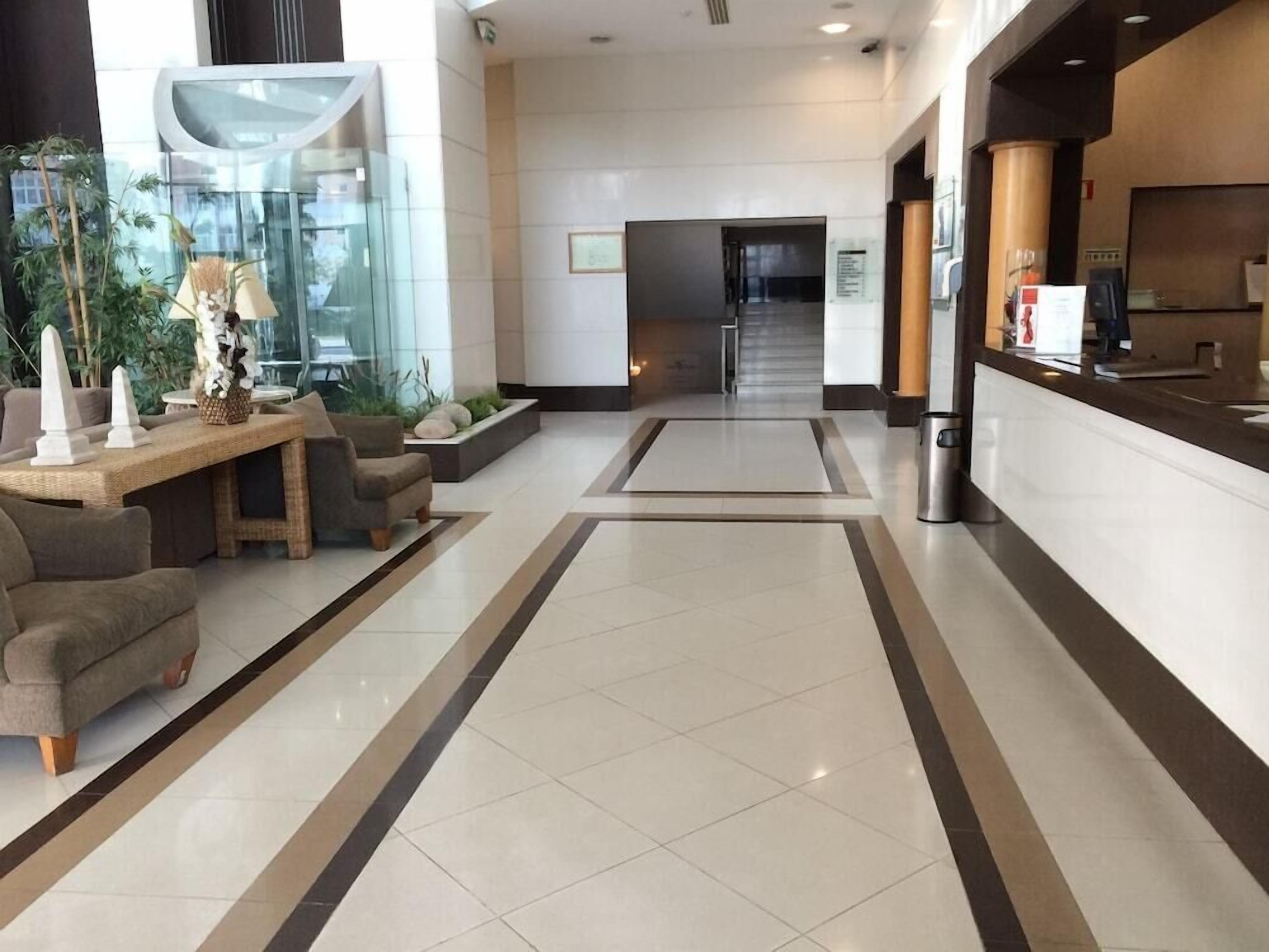 A hotel lobby with a reception desk, seating area, and a glass wall with plants.