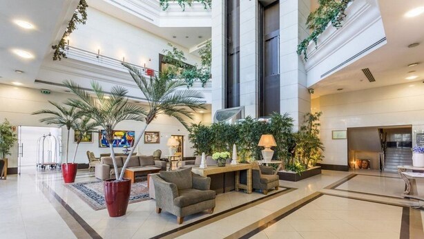 Eine großzügige Lobby mit hoher Decke, verschiedenen Sitzbereichen und Zimmerpflanzen.