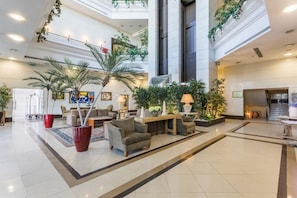 Un hall amplio con techo alto, varias zonas de estar y plantas de interior.