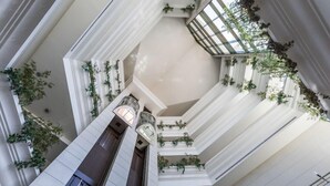 Ein mehrgeschossiges Atrium mit einem zentralen Aufzug, weißen Wänden und Bepflanzung an den Balkonen.