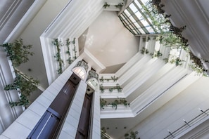 A multi-level atrium with a central elevator, white walls, and greenery on balconies. - Riviera Hotel Carcavelos (Cascais)