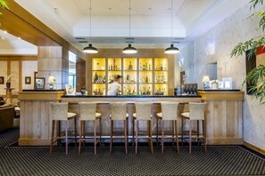 A bar area with a counter, bar stools, and shelves of bottles. - Riviera Hotel Carcavelos (Cascais)