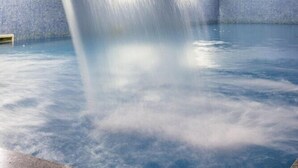 Ein moderner Innenpool mit Wasserfall, gefliesten Wänden und einem klaren, blauen Beckenboden.