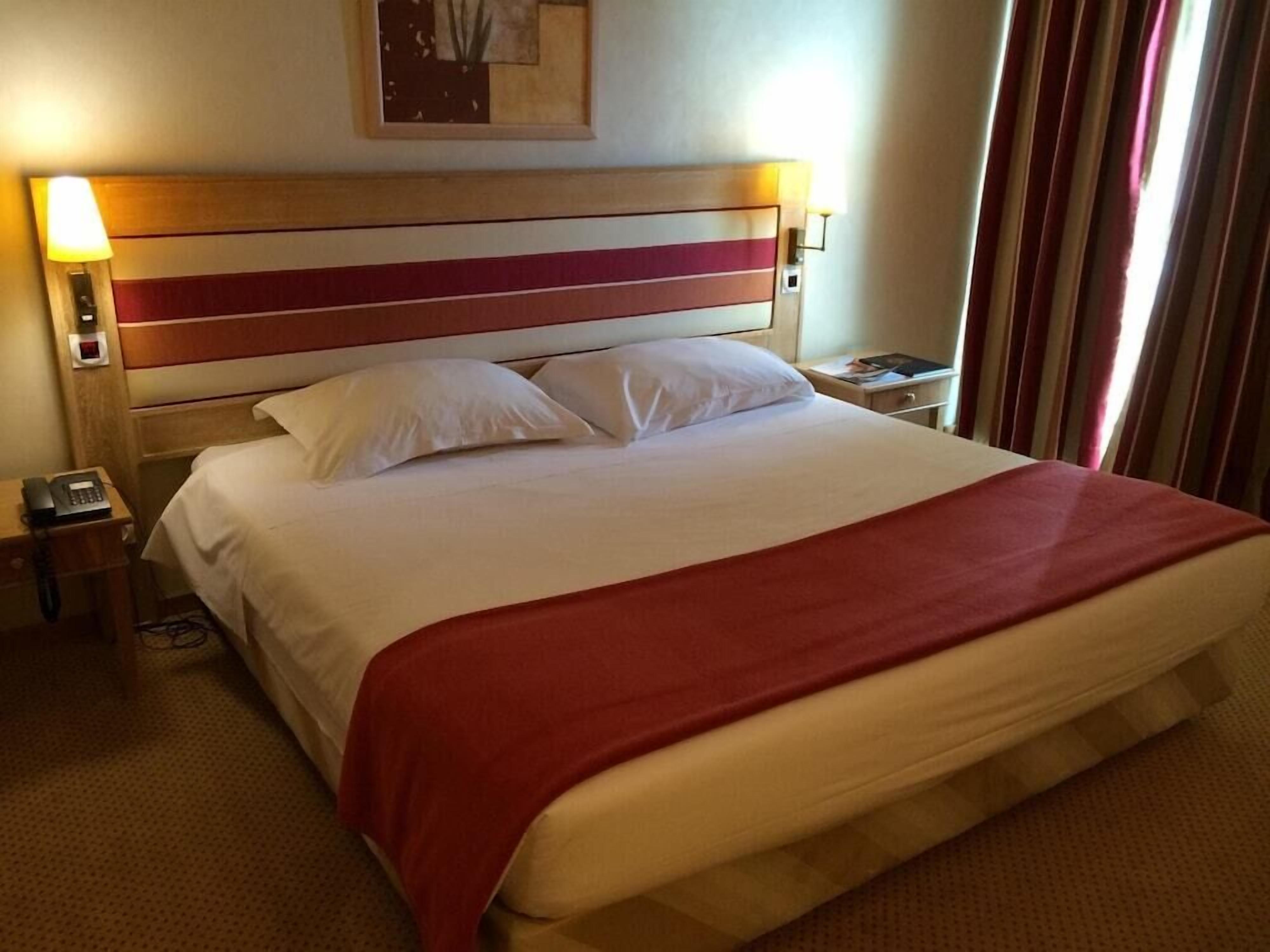 Una habitación de hotel con cama, mesita de noche, lámpara y una obra de arte colgada en la pared.