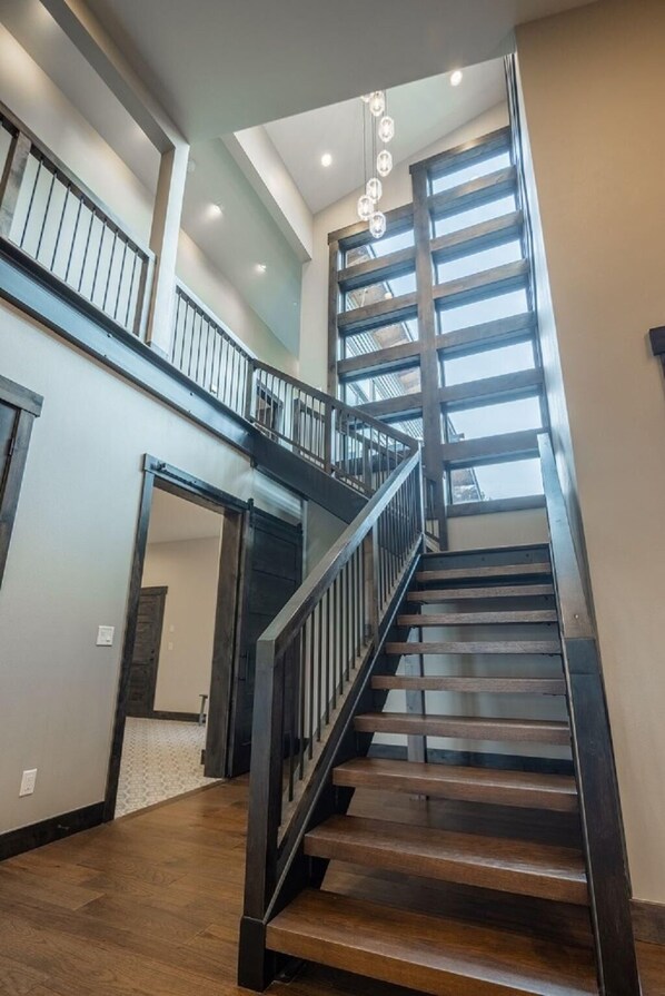 A modern staircase with wooden steps and metal railings, leading to a balcony with large windows.