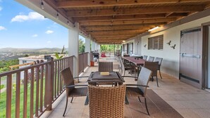 Une terrasse extérieure dotée d'un plafond en bois, de chaises et de tables en osier, offrant une vue imprenable sur un paysage magnifique.