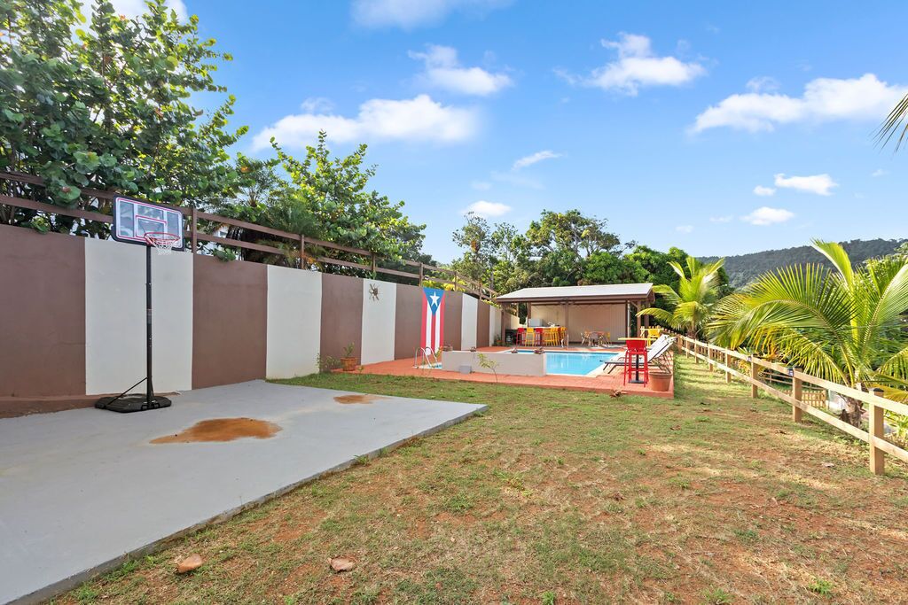 Un patio trasero con aro de baloncesto, piscina y valla de madera.