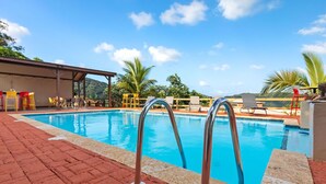 Une piscine avec des échelles en métal, entourée d’une terrasse en briques rouges et de mobilier d’extérieur.