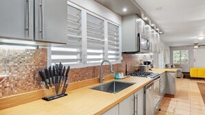 Une cuisine moderne dotée d’un plan de travail en bois, d’appareils électroménagers en acier inoxydable et d’une fenêtre avec des stores.