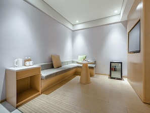 A modern, compact room with a built-in sofa, a small round table, a coffee station, and a mini-fridge.