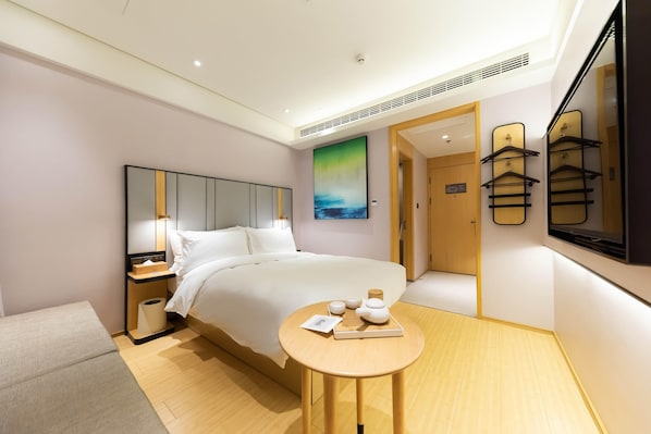 A hotel room with a bed, bedside table, and a painting on the wall.