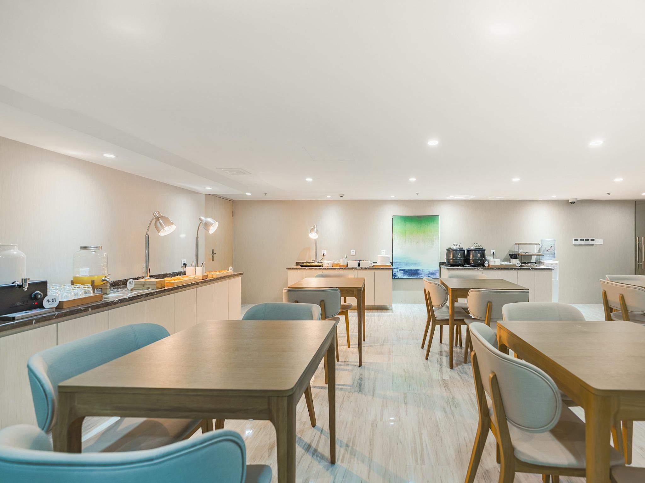A modern hotel room with a dining area, kitchen, and a large window with a view.