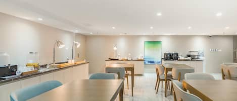A modern hotel room with a dining area, kitchen, and a large window with a view.