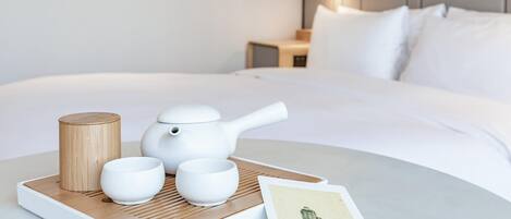 Un juego de té ordenado sobre una bandeja con base de madera, colocado sobre una cama con ropa blanca.