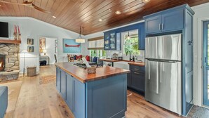 A modern kitchen with blue cabinets, a large island, and a stainless steel refrigerator. - Linger Longer: One-Level Luxury Home w/ Screened Porch, 2 Fireplaces, Firepit (Highlands)