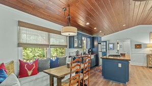 A cozy kitchen with wooden ceiling, a dining area with a wooden table and chairs, and a built-in island with a sink. - Linger Longer: One-Level Luxury Home w/ Screened Porch, 2 Fireplaces, Firepit (Highlands)