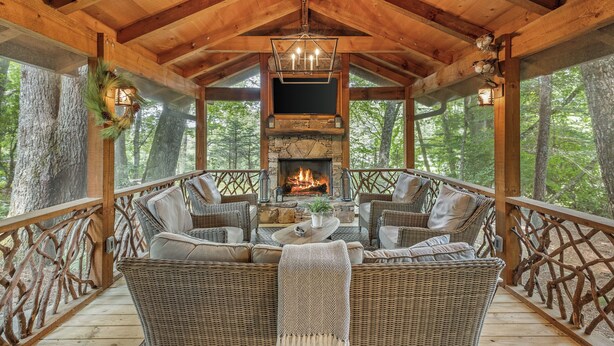 A covered outdoor seating area with wicker furniture, a stone fireplace, and a wooden ceiling. - Linger Longer: One-Level Luxury Home w/ Screened Porch, 2 Fireplaces, Firepit (Highlands)