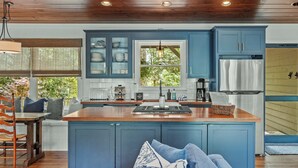 A kitchen with blue cabinets, a wooden island, and a window with a view of trees. - Linger Longer: One-Level Luxury Home w/ Screened Porch, 2 Fireplaces, Firepit (Highlands)