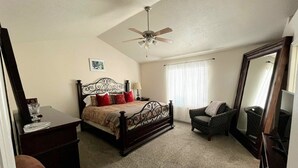 A bedroom with a bed, a chair, a dresser, a ceiling fan, and a large mirror.