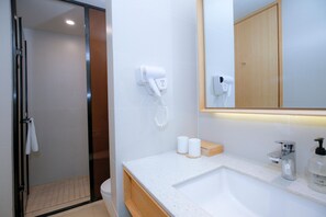 Un baño moderno con un lavamanos blanco, un espejo y dos secadores de pelo montados en la pared.