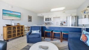 Una sala de estar moderna con un sofá, una mesa de centro y un televisor mostrando un anuncio de vacaciones.