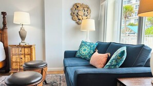 Una sala de estar con un sofá azul, cojines estampados, un adorno de pared y una mesita de madera.